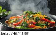 Hot steaming grilled vegetables, carrot, green bean, broccoli, pepper. Serving a white plate on wooden table desk, black wall background. Boiled food healthy meal concept. Ratatouille with smoke steam. Стоковое AI-видео, аниматор Марина Демидюк / Фотобанк Лори
