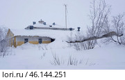 An old snow-covered building in Vorkuta, partially covered with snowdrifts. It is clear that the snow has accumulated up to the first-floor windows, almost completely hiding the lower part of the building. The roof is covered with a thick layer of snow, and dry bushes covered with snow are located nearby.A tall antenna is installed on the roof of the building, which may indicate its past administrative or industrial significance. Perhaps this is an old headquarters, mine administration, or utility facility. The walls of the building are painted yellowish-gray, which contrasts with the whiteness of the snow and the gray sky.Judging by the condition of the windows, facade, and snowdrifts, the building is either abandoned or used very rarely. The photograph perfectly conveys the atmosphere of the harsh polar winter in Vorkuta. Стоковое фото, фотограф Анна Кривицкая / Фотобанк Лори