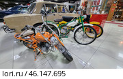 Retro vehicles from the Soviet era, displayed in the USSR Museum. The focus is on mopeds, motorcycles and a Soviet car.An orange mini-motorcycle with a low frame, compact design and a front headlight fairing.A green moped with a motor reminiscent of models like "Riga" or "Karpaty". It has a characteristic design of a bicycle with an engine.A yellow moped with chrome parts and a retro design.A Soviet car "Zhiguli" (VAZ-2101 or VAZ-2103) in beige with a chrome bumper.Retro motorcycles in the far corner with characteristic features of Soviet motor vehicles.An exhibition of items from the Soviet era, including awards, banners and rare books. (2023 год). Редакционное фото, фотограф Анна Кривицкая / Фотобанк Лори
