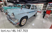 Classic Soviet car "Moskvich-407", located in the USSR museum. This car was produced by the Moscow Plant of Small Cars (AZLK) from 1958 to 1963. The car is painted light blue with characteristic chrome details, such as the radiator grille, bumpers and mirrors.The "Moskvich-407" car is a classic of the Soviet automobile industry.Light blue body color, shiny chrome details.Retro hubcaps on the wheels, branded "Moskvich" emblems.Nearby is another Soviet car, probably "Pobeda" GAZ-M20.Display cases with antiques - old watches, household items of the USSR.A Soviet-made motorcycle on the right side of the frame.An exposition dedicated to the USSR, with items of the era. (2023 год). Редакционное фото, фотограф Анна Кривицкая / Фотобанк Лори