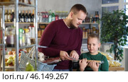 Man shows his son a list of groceries in a supermarket. Child helps the father choose and buy food. Стоковое видео, видеограф Яков Филимонов / Фотобанк Лори