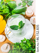 Fresh herbs and vegetables surround a glass of minty beverage on a wooden kitchen table. Стоковое фото, фотограф Сергей Толмачёв / Фотобанк Лори