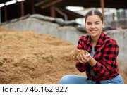Young woman farmer holding beer oilcake in hands in fodder storage. Стоковое фото, фотограф Яков Филимонов / Фотобанк Лори
