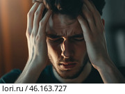 Young man holds his head in distress, coping with overwhelming stress and feelings of anxiety in a dimly lit room during the evening. Стоковое AI-изображение, AI-художник Sergey Grishin / Фотобанк Лори