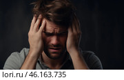 A young man experiences overwhelming stress, gripping his head tightly with both hands as he battles his emotions in a dark, moody setting, reflecting his inner turmoil. Стоковое AI-изображение, AI-художник Sergey Grishin / Фотобанк Лори