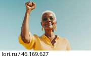 Black mature woman outdoors with raised fist of empowerment, strength and women solidarity, International Womens Day, Black History Month concept. Стоковое AI-изображение, AI-художник Анастасия Золотницкая / Фотобанк Лори