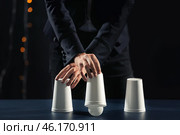 Magician showing tricks with cups on dark background. Стоковое фото, фотограф Pixel_shot / Фотобанк Лори