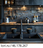 Stylish kitchen in industrial design with dark tones. The central place is occupied by a black sink with a modern matte mixer. On its side there are two dark ceramic mugs with aromatic coffee, which adds a cozy atmosphere.The kitchen background is made in the loft style with brickwork, metal elements and industrial lamps. In the background you can see a kettle, a saucepan, spices in glass jars, as well as hanging kitchen utensils. The lighting creates soft warm accents against the background of cold metal surfaces.The overall style of the kitchen combines the brutality of industrial design with cozy elements, creating a modern and stylish atmosphere. Стоковое AI-изображение, AI-художник Анна Кривицкая / Фотобанк Лори