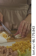 A housewife is carefully slicing a boiled egg on a cutting board in her cozy, rustic kitchen. Стоковое видео, видеограф Strunov David / Фотобанк Лори
