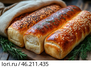 A mouth-watering image of freshly baked bread with a golden, crisp crust. Three fragrant loaves are laid out on a wooden board and decorated with various toppings: sesame seeds, flax seeds and herbs. Their soft, airy texture is visible thanks to a cut in one of the loaves. Sprigs of fresh dill and rosemary are placed around, giving the photo a rustic, homely feel. Burlap fabric is visible in the background, complementing the atmosphere of naturalness and traditional baking. Стоковое AI-изображение, AI-художник Анна Кривицкая / Фотобанк Лори