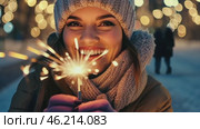 Smiling Girl with Fire Sparkler Glow in the Winter Season. pleased happy smiling young 20s woman is holding a bright sparkler in a festive winter setting. Glowing blur bokeh light on background. Стоковое AI-видео, аниматор Марина Демидюк / Фотобанк Лори