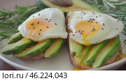 Modern Two Toasts with avocado and fried egg Spreading Yolk, rosemary 4K. Preparing healthy toast breakfast avocado slices rye wholegrain bread, sunny side up egg on top. breakfast for two, couple. Стоковое видео, видеограф Елизавета Малкова / Фотобанк Лори