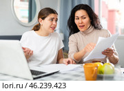 Two women with financial documents near laptop sitting at table at home. Стоковое фото, фотограф Яков Филимонов / Фотобанк Лори