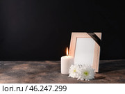 Blank funeral frame, candle and flowers on table against black background. Стоковое фото, фотограф Pixel_shot / Фотобанк Лори