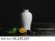 Mortuary urn with ribbon and flower on table against dark background. Стоковое фото, фотограф Pixel_shot / Фотобанк Лори