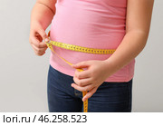 Overweight girl measuring her waist on light background. Стоковое фото, фотограф Pixel_shot / Фотобанк Лори