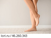 Woman suffering from pain in leg while standing near light wall. Стоковое фото, фотограф Pixel_shot / Фотобанк Лори