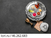 Passover Seder plate with traditional food, cup, matza and kippah on dark background. Стоковое фото, фотограф Pixel_shot / Фотобанк Лори