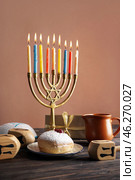Menorah with doughnut, jug and dreidels for Hannukah celebration on table near brown wall. Стоковое фото, фотограф Pixel_shot / Фотобанк Лори