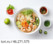 A delicious bowl of Asian soup with rice noodles and shrimp. The dish is decorated with fresh vegetables: cucumbers, herbs, lettuce, lime wedges. Additional ingredients are also placed next to the plate: sliced ​​red chili pepper, soy sauce with green onions, chopped cilantro and green pepper wedges. The combination of bright colors, fresh products and neat presentation makes the composition aesthetically attractive. Стоковое AI-изображение, AI-художник Анна Кривицкая / Фотобанк Лори