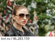 With confidence radiating, a young woman wearing sunglasses stands elegantly, showcasing her leather jacket, amidst a lively backdrop filled with colorful art. Стоковое фото, фотограф Aleksandr Golubev / Фотобанк Лори
