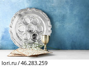 Passover Seder plate with cup of wine and matza on table against color background. Стоковое фото, фотограф Pixel_shot / Фотобанк Лори