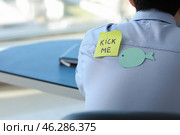 Sticky note with text KICK ME and paper fish on back of man working in office. April Fools' Day prank. Стоковое фото, фотограф Pixel_shot / Фотобанк Лори