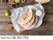 Board with tasty quesadillas, lime and sauces on wooden background. Стоковое фото, фотограф Pixel_shot / Фотобанк Лори
