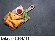 Board with tasty Uzbek samsa and tomato sauce on dark background. Стоковое фото, фотограф Pixel_shot / Фотобанк Лори