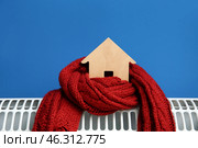 Figure of house with warm scarf on electric convector heater near blue wall at home. Heating saving concept. Стоковое фото, фотограф Pixel_shot / Фотобанк Лори