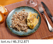 Prepared buckwheat porridge with piece of fried chicken is served on large white platter with bread. Стоковое фото, фотограф Яков Филимонов / Фотобанк Лори