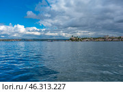 Picturesque seascape of Sevastopol Bay. In the foreground is a smooth water surface reflecting the sky and clouds. In the distance on the horizon is visible the coast with city buildings, green spaces and port facilities.On the right, on the hill, historical buildings are visible, probably one of the iconic objects of Sevastopol. Voluminous clouds hang over the city, creating an atmosphere of maritime climate, changeable weather and natural grandeur. The picture conveys the spirit of the sea city, its connection with history, navy and nature. Стоковое фото, фотограф Анна Кривицкая / Фотобанк Лори