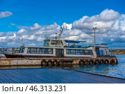 Passenger boat "Ecoid" moored to the pier in Sevastopol. The vessel has a classic design for water transport of this region: an elongated hull with rows of windows, an upper deck with an open space and a canopy, as well as a wheelhouse with equipment. A lifebuoy is visible on board, and the boat is moored to the pier with thick ropes. In the background, you can see residential buildings of the city and a picturesque sky with snow-white clouds. (2021 год). Редакционное фото, фотограф Анна Кривицкая / Фотобанк Лори