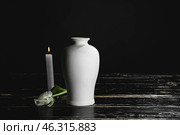 Mortuary urn with burning candle and flower on table against dark background. Стоковое фото, фотограф Pixel_shot / Фотобанк Лори