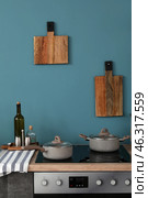 Electric stove with cooking pots and cutting boards hanging on blue wall in modern kitchen. Стоковое фото, фотограф Pixel_shot / Фотобанк Лори