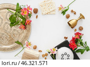 Frame made of Passover Seder plate, flatbread matza, kippah, wine cup, walnuts and flowers on white background. Стоковое фото, фотограф Pixel_shot / Фотобанк Лори