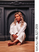 Inside a tastefully decorated room, a middle-aged woman sits thoughtfully in a relaxed pose. With her bare feet tucked beneath her, she embodies a moment of introspection against a rich backdrop. Стоковое фото, фотограф Aleksandr Golubev / Фотобанк Лори