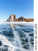 Scenic winter landscape of frozen Baikal Lake. View of famous Shamanka Rock - natural landmark of Olkhon Islands from blue clear ice with cracks on sunny day of February. Winter travels and recreation. Стоковое фото, фотограф Виктория Катьянова / Фотобанк Лори