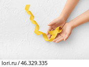 Hands with golden ribbon on white background. Childhood cancer awareness concept. Стоковое фото, фотограф Pixel_shot / Фотобанк Лори