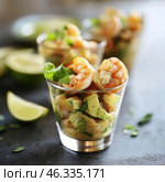 A sophisticated dish – shrimp cocktail served in a glass. The main ingredients include juicy, lightly fried shrimp with seasonings, slices of fresh avocado, aromatic cilantro and perhaps other ingredients such as lime or mango. In the background you can see additional servings of this dish, as well as lime wedges, which hint at the freshness and lightness of the presentation. The dark background creates a beautiful contrast with the bright colors of the food, making the image especially appetizing. Стоковое AI-изображение, AI-художник Анна Кривицкая / Фотобанк Лори
