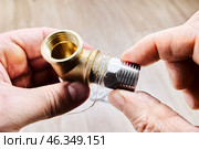 Hex nipple barrel reducer adapter is being sealed with plumbing hemp and screwed into brass elbow fitting, ensuring secure threaded joint in pipe fitting. Стоковое фото, фотограф Владимир Григорьев / Фотобанк Лори