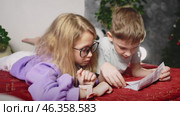 Curious children explore smartwatch functions while lying on bed. Girl in glasses attentively taps smartwatch screen, showing features to friend. Concept of kids learning technology interactive play. Стоковое видео, видеограф Енваев Андрей / Фотобанк Лори