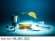 Glass of rum with ice cubes, lemon slice, tongs and jigger on dark blue background. Стоковое фото, фотограф Pixel_shot / Фотобанк Лори