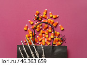 Shopping bag with tasty candy corns, Halloween decor and skeleton hand on pink background. Стоковое фото, фотограф Pixel_shot / Фотобанк Лори