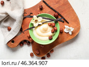 Wooden board with ramekin of tasty vanilla pudding and hazelnuts on light background, closeup. Стоковое фото, фотограф Pixel_shot / Фотобанк Лори
