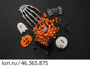 Shopping cart with tasty candy corns, skeleton hand and cookies for Halloween on black background. Стоковое фото, фотограф Pixel_shot / Фотобанк Лори