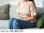 Young woman sitting on sofa and suffering from abdominal pain at home. Стоковое фото, фотограф Pixel_shot / Фотобанк Лори