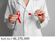 Doctor holding HIV blood test tube and red ribbon on grey background. Стоковое фото, фотограф Pixel_shot / Фотобанк Лори