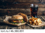 French fries, burger, pork ribs on a stylish board on a wooden background. Fried potatoes. The concept of fast food, junk food and fast food preparation. Стоковое AI-изображение, AI-художник Photojuli / Фотобанк Лори