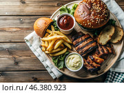 French fries, burger, pork ribs on a stylish board on a wooden background. Fried potatoes. The concept of fast food, junk food and fast food preparation. Стоковое AI-изображение, AI-художник Photojuli / Фотобанк Лори